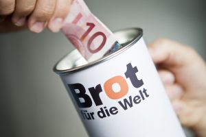 Spendendose von Brot für die Welt und eine Hand, die einen 10-Euro-Schein hineinsteckt (Copyright: Hermann Bredehorst / Brot für die Welt)