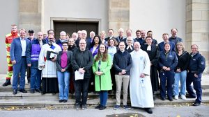 Viele Menschen (ca. 40) stehen vor einer Kirche und lächeln in die Kamera, unter ihnen einige im Talar, mit den violetten Westen der Notfallseelsorge, in Uniformen von Polizei und Rettungsdiensten. Foto: Ernst Alexander Biedermann