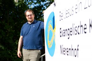 Christian Jünner neben dem Hinweisschild zur evangelischen Kirchengemeinde Nierenhof
