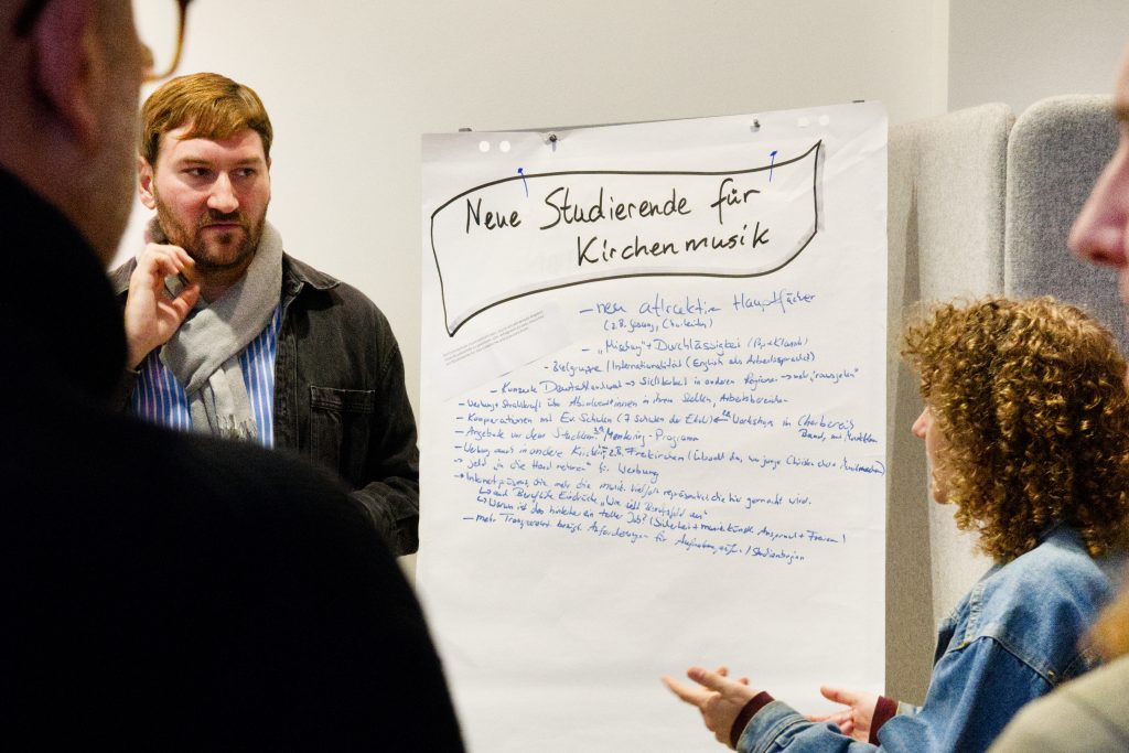 Ein junger Mann (links) und eine junge Frau (rechts) im Gespräch während der Arbeitsphase. Im Hintergrund ein beschriebenes Flipchart (Foto: Hans-Martin Julius)