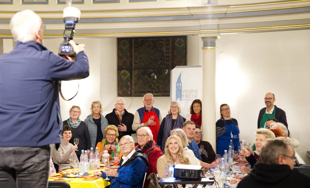 Ein Fotograf steht auf einem Stuhl und fotografiert die Gruppe der Förderinnen und Förderer der Vesperkirche (Foto: Hans-Martin Julius)