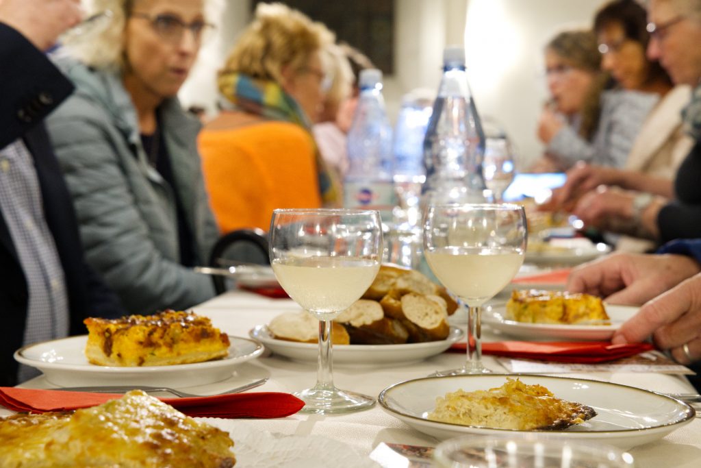 Menschen beim Essen und im Gespräch. Im Vordergrund Teller mit Zwiebelkuchen und gefüllte Gläser (Foto: Hans-Martin Julius)