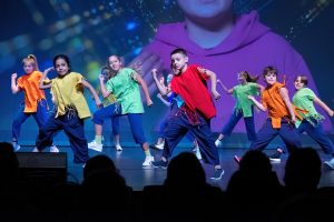 Acht Kinder vom Tanztheater tanzen auf der Bühne, im Hintergrund ist ein Video mit einem Kind zu sehen (Foto: Tanztheater Abrakadabra)